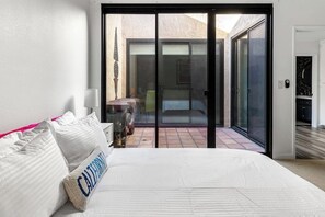 A bedroom with a bed, a pillow, a nightstand, and a sliding glass door leading to a patio area. - Stylish Palm Springs Retreat with Pool (Palm Springs)
