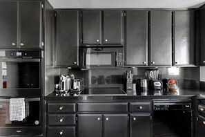 A modern kitchen with dark cabinetry, stainless steel appliances, and a central island. - Stylish Palm Springs Retreat with Pool (Palm Springs)