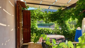 A covered patio with a table and chairs, surrounded by lush green vines and a view of the countryside. - 2-Room apartment with terrace overlooking the sea, private parking (Rio)