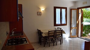 A compact kitchen with a gas stove, sink, and a dining table with chairs. There is a window with curtains and a door leading to an outdoor area. - 2-Room apartment with terrace overlooking the sea, private parking (Rio)
