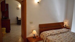 A bedroom with a wooden headboard, a bedside lamp, a patterned bedspread, and a nightstand with a lamp. - 2-Room apartment with terrace overlooking the sea, private parking (Rio)