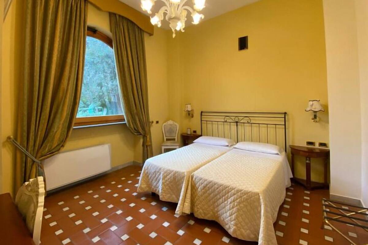 Ein Schlafzimmer mit zwei Betten, einer Chandelier, einem Fenster mit Vorhängen und einer Heizung.