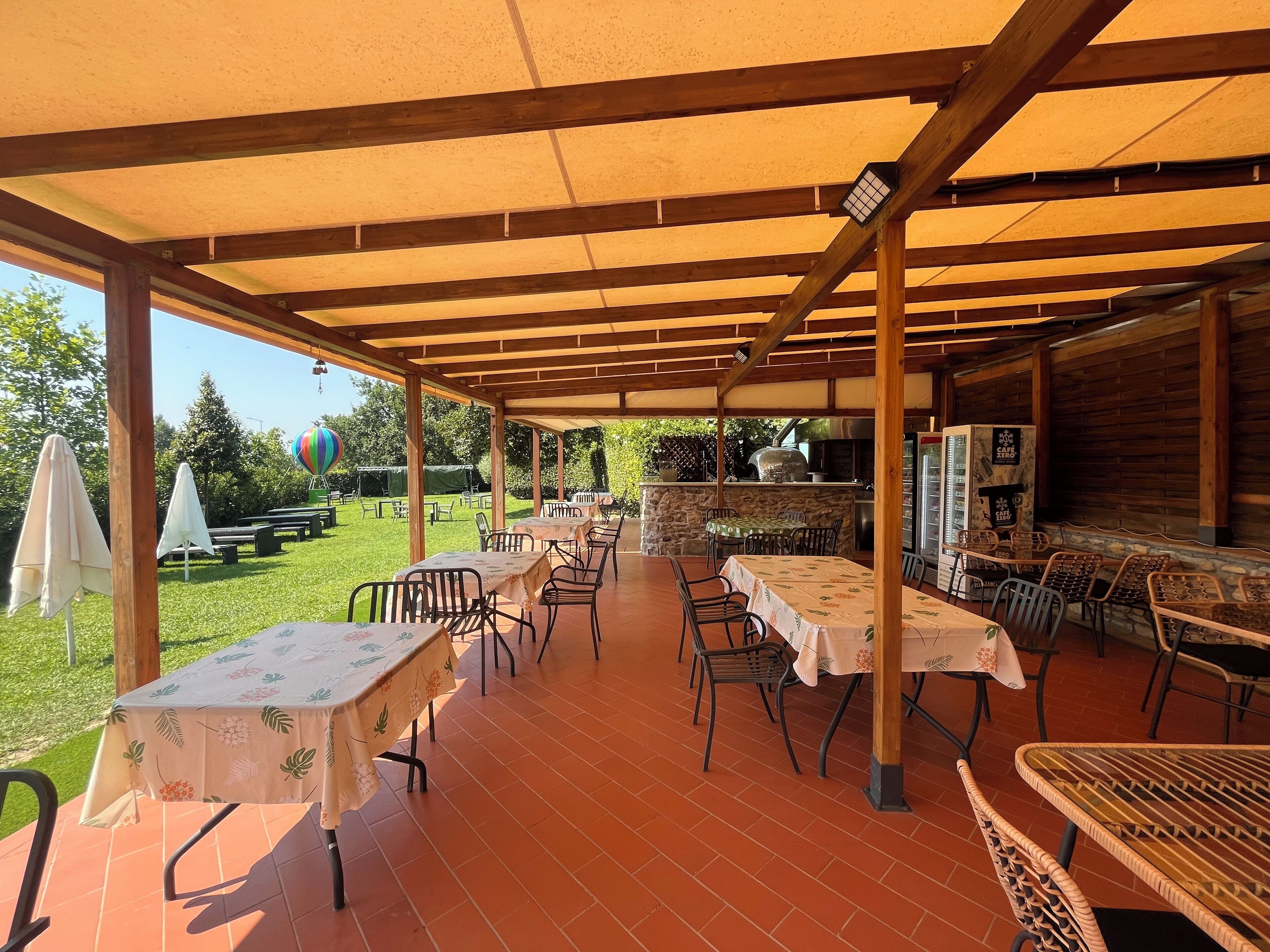 Un patio al aire libre con mesas, sillas, una parrilla y vistas al jardín.