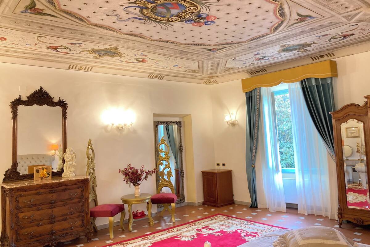 Ein Zimmer mit aufwendigen Zierelementen an der Decke, einem großen Spiegel und einem roten Teppich.