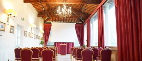 A conference room with rows of red chairs, a wooden ceiling, and a projector screen.