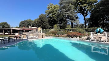 Piscina azul cristalina con sillas de descanso y una estatua, rodeada de árboles y un jardín.