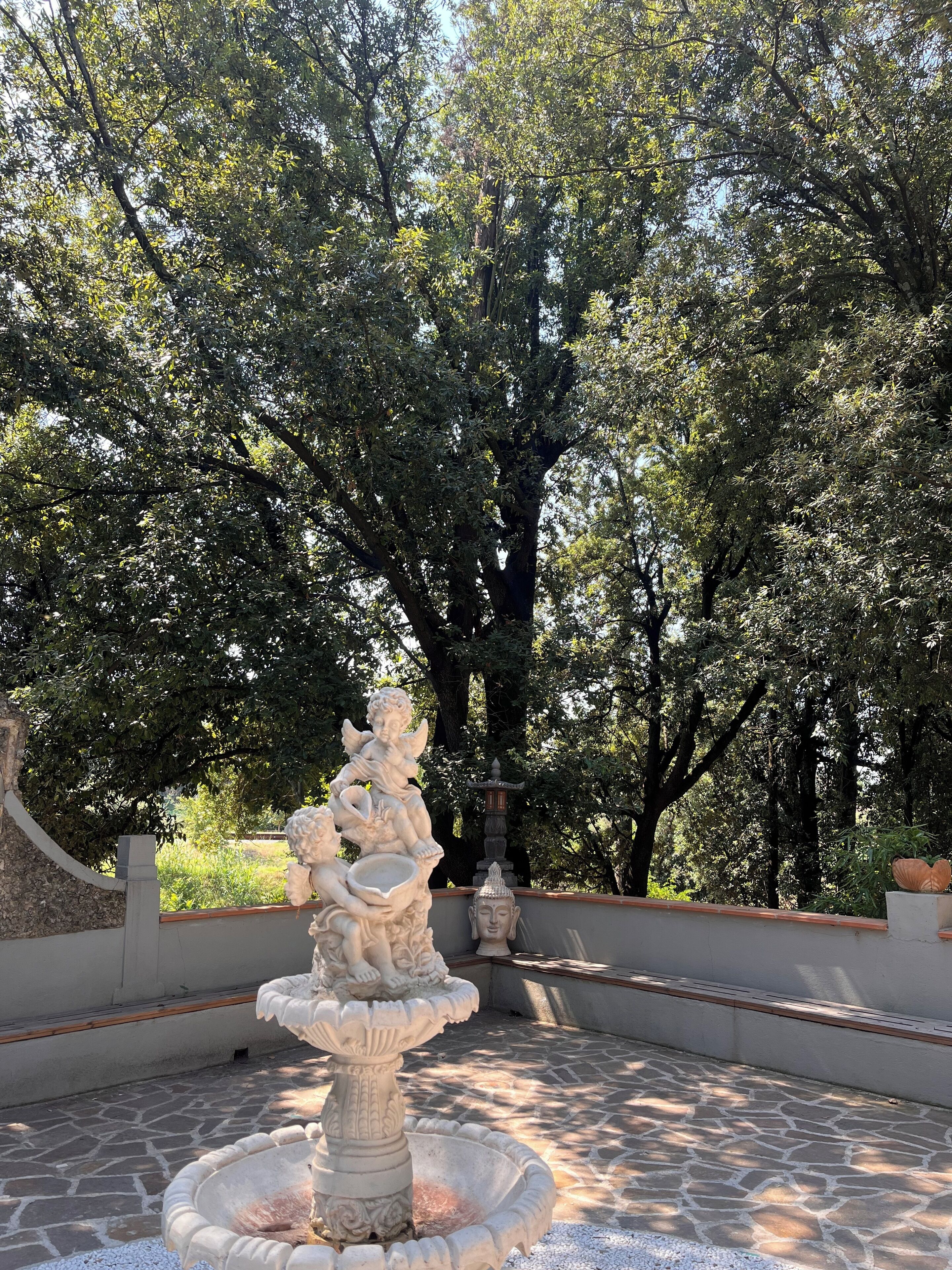 A stone fountain with a seated figure, surrounded by trees.