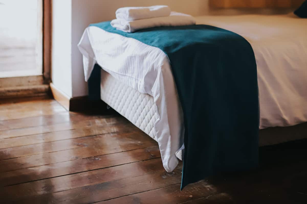 Ein Zimmer mit einem Bett, Holzboden, einem Fenster mit Vorhängen und einer Tür.
