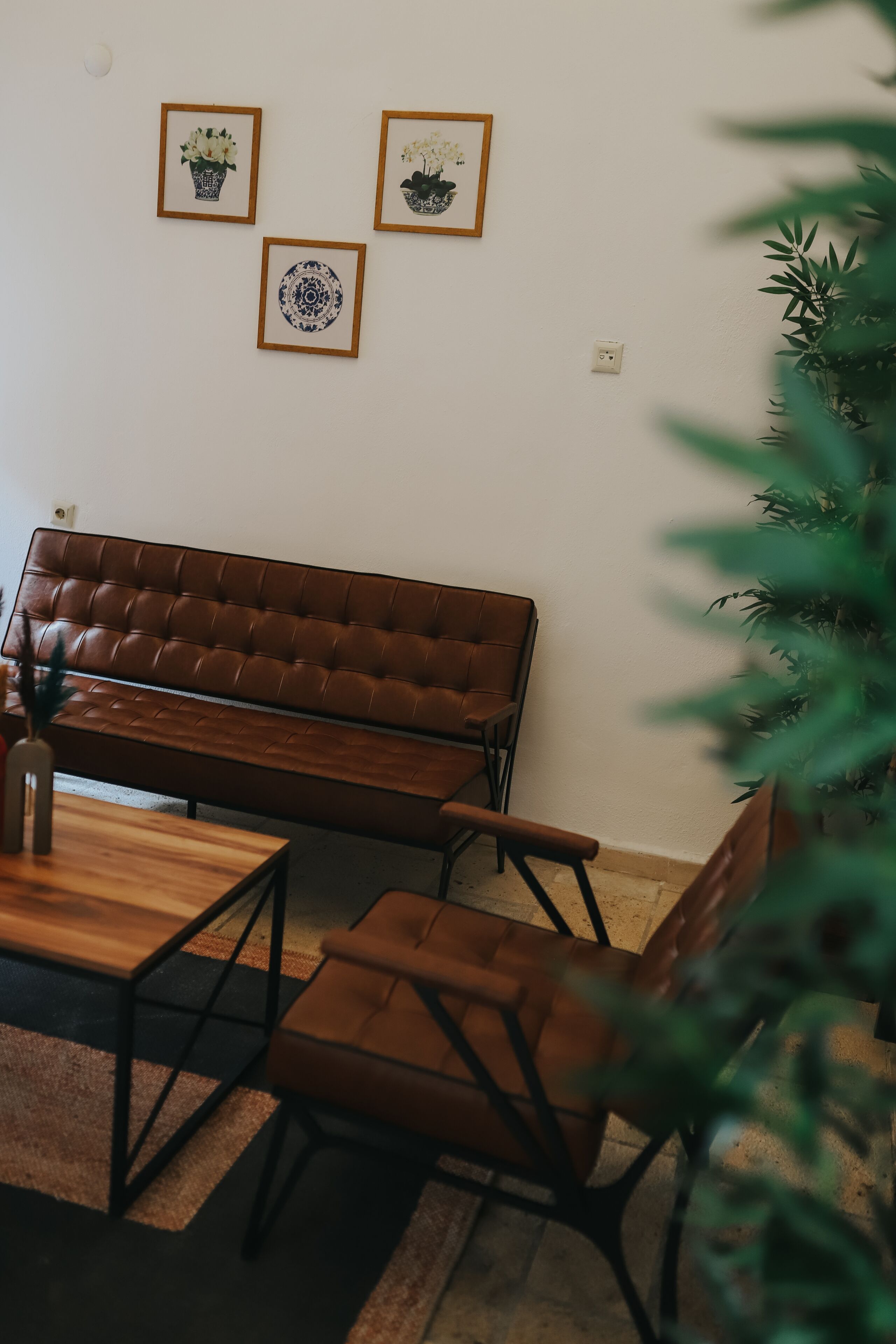 A brown leather sofa, a wooden coffee table, and two matching armchairs in a room with a white wall and three framed pictures.