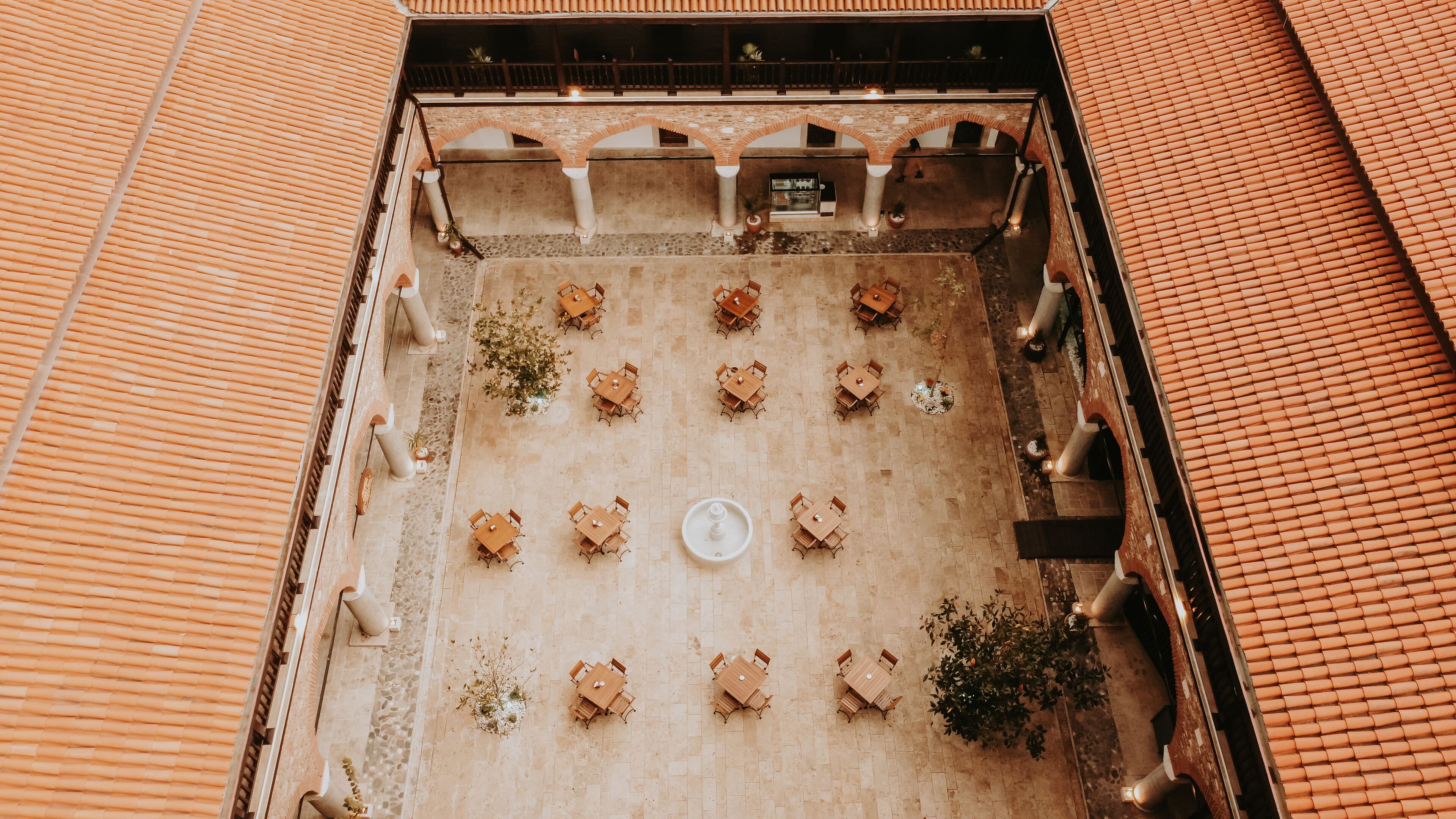 An aerial view of a courtyard with multiple tables and chairs arranged in a grid pattern, surrounded by brick walls and columns.