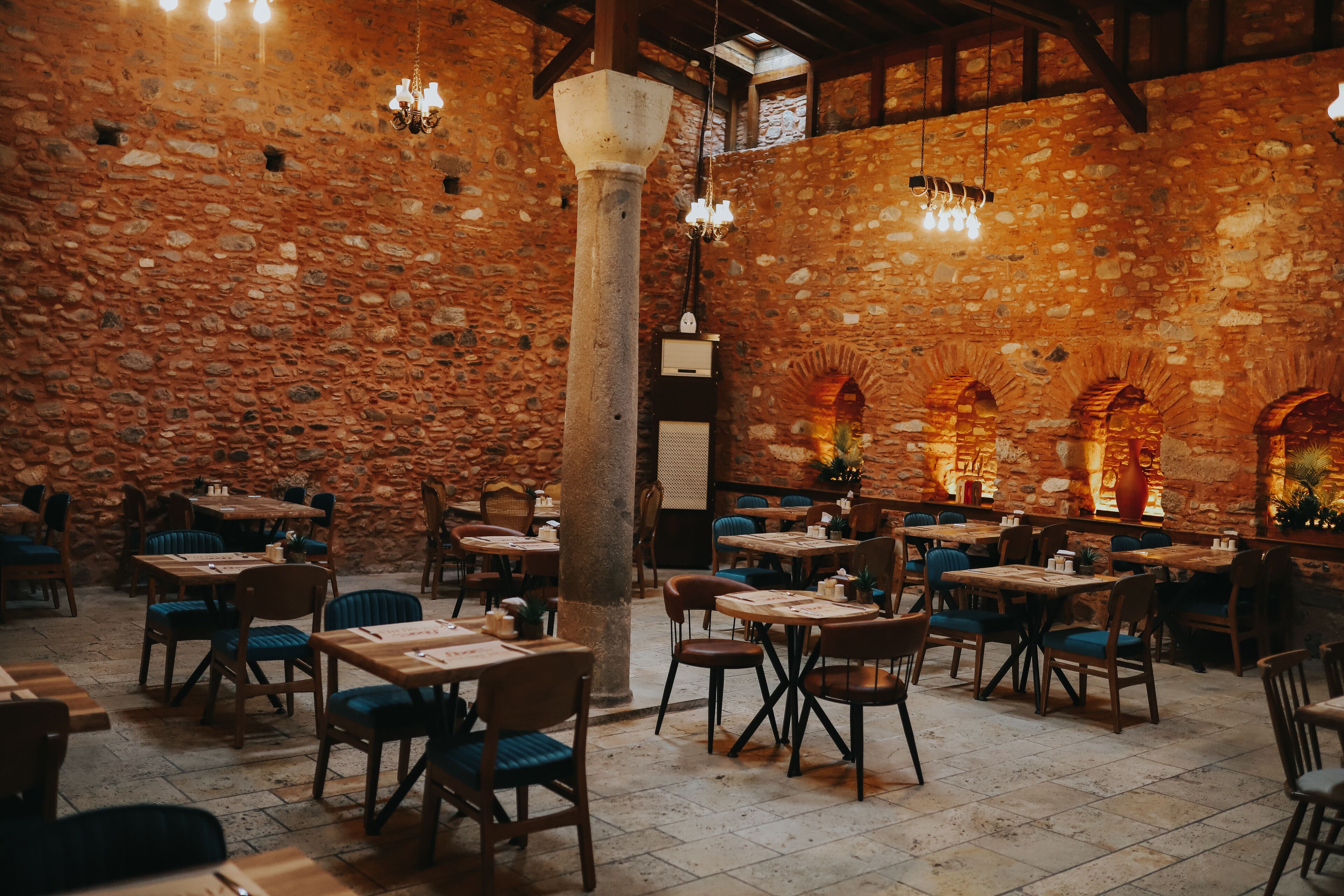 Un restaurant aux murs de pierre, aux tables en bois et aux chaises bleues.