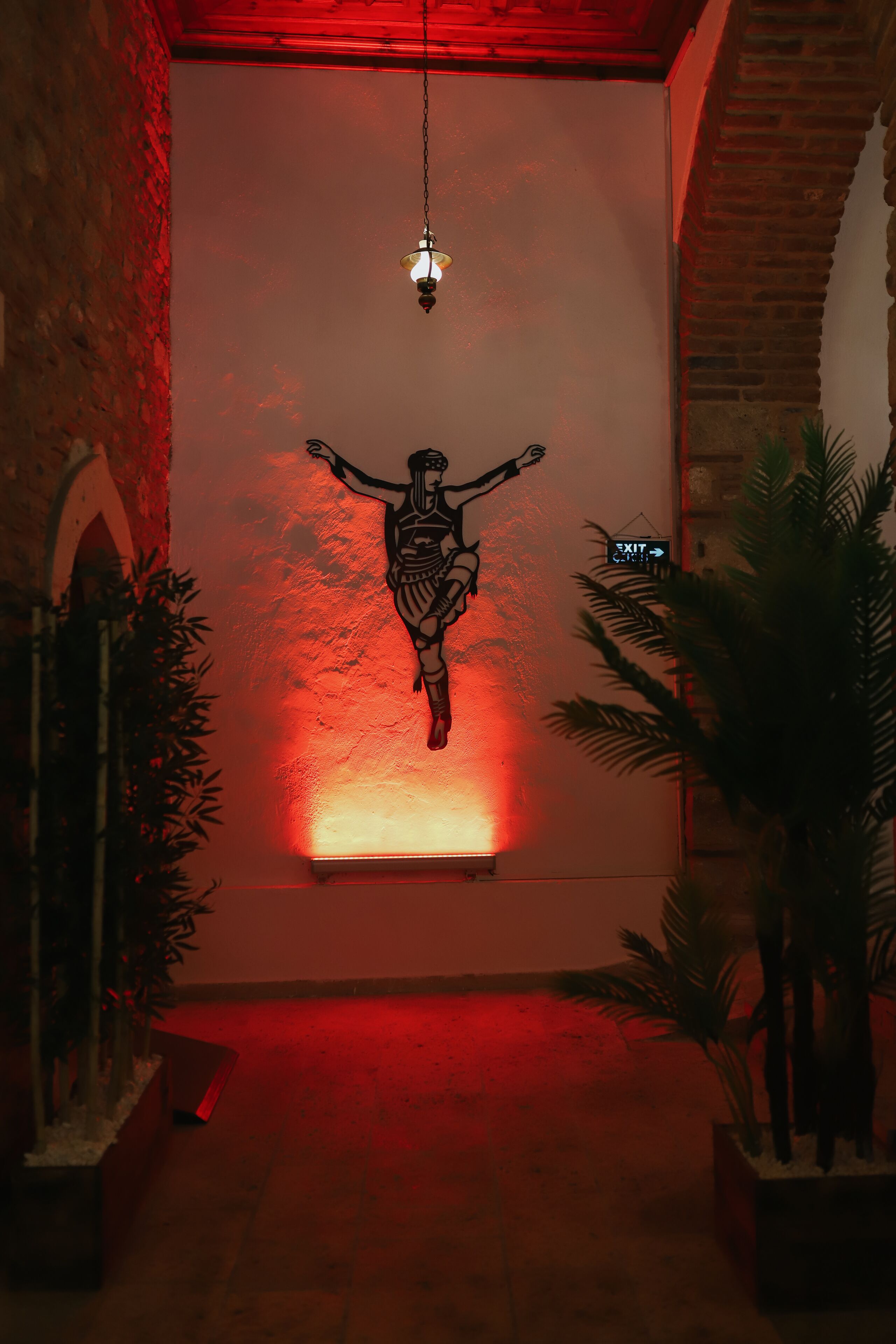 A hallway with a red-lit wall, a hanging light fixture, and a wall-mounted sign.