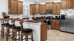 A modern kitchen with wooden cabinets, stainless steel appliances, and a central island with bar stools. - Free Baby Amenities! Stunning Disney Themed Villa! Game Room, Sunny Pool & Spa (Davenport)