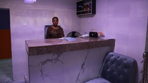 Un comptoir d’accueil avec un revêtement en marbre, une chaise noire rembourrée et une étagère contenant divers objets.