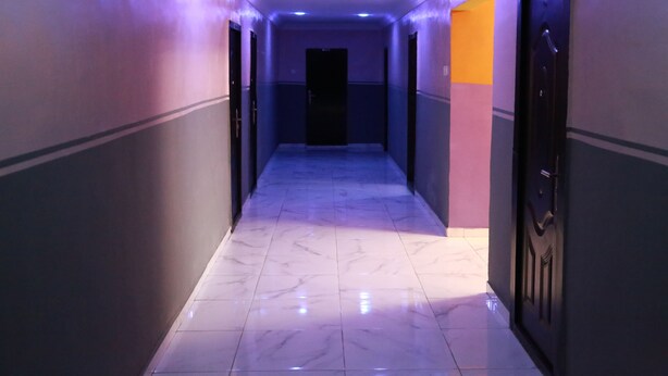 Un couloir au sol de marbre, avec des portes de chaque côté et une porte sombre au fond.