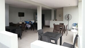 Un vaste espace de vie comprenant une table et des chaises, un coin cuisine avec un évier et un ventilateur, ainsi qu’un téléviseur à écran plat fixé au mur.
