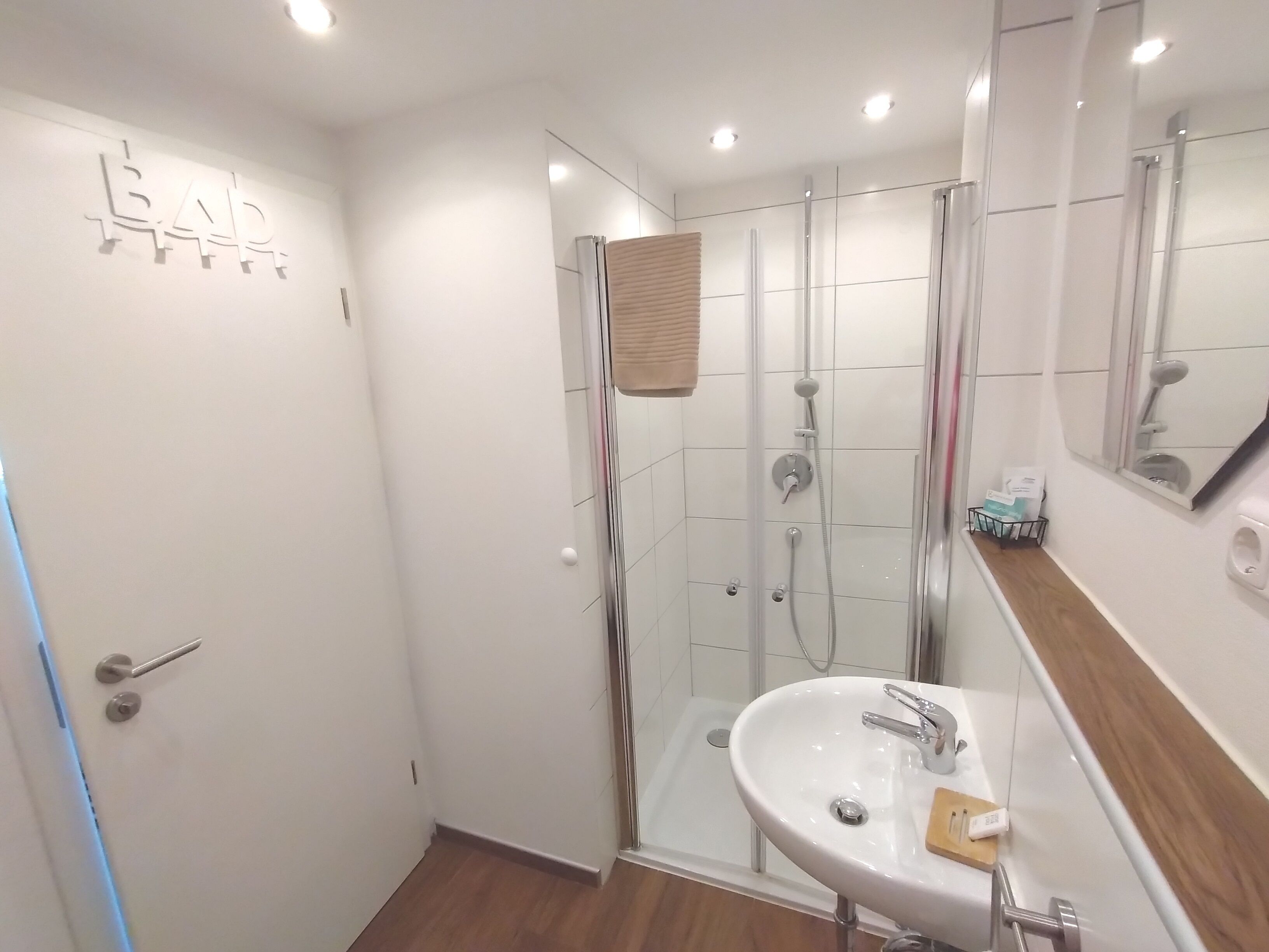 Un baño moderno con ducha de vidrio, lavamanos blanco y un espejo encima.