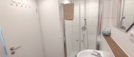 Un baño moderno con ducha de vidrio, lavamanos blanco y un espejo encima.