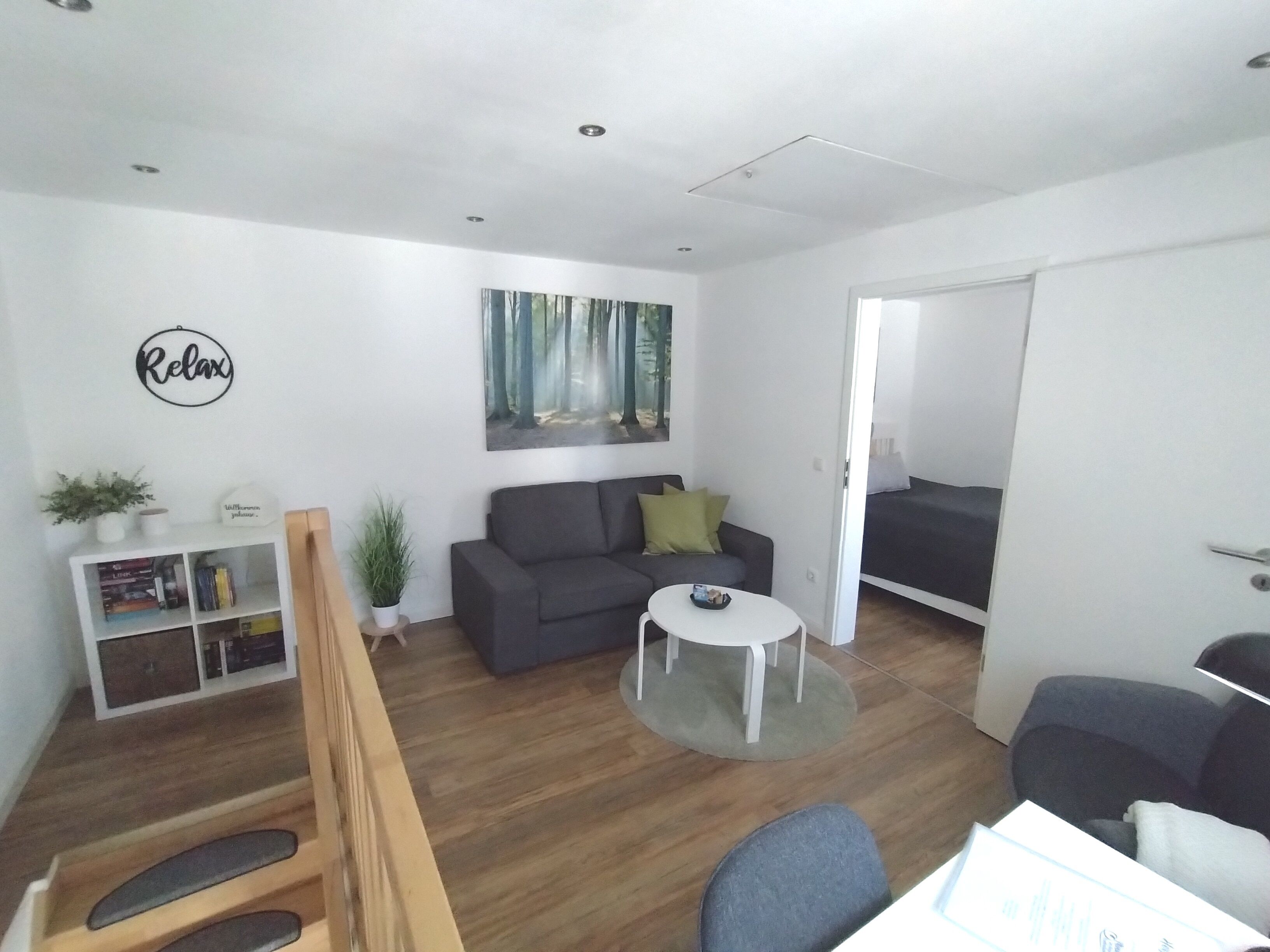 Een moderne woonkamer met een grijze bank, een bijzettafeltje en een boekenkast.