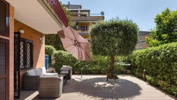 Eine Terrasse mit Gartenmöbeln, einem großen Sonnenschirm und einem Baum.