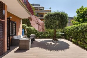 Eine Terrasse mit Gartenmöbeln, einem großen Sonnenschirm und einem Baum.