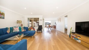 A spacious living area with a blue sofa, a glass coffee table, and a TV on a wooden stand.