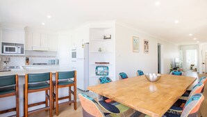 A modern kitchen with white cabinets, a microwave, and a stove. There is a dining area with a wooden table and colorful chairs.