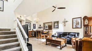 A spacious living room with a staircase, a chandelier, a dining area, and a black leather sofa.