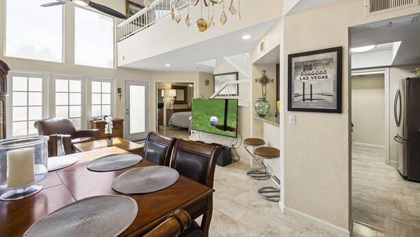 A spacious living area with a high ceiling, a chandelier, a television, and a dining table with chairs.