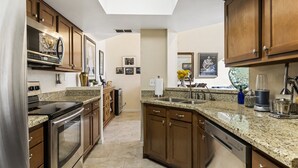 A modern kitchen with granite countertops, stainless steel appliances, wooden cabinets, and a skylight.