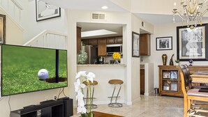 A living room with a flat-screen TV, a coffee table, and a dining area with a chandelier.