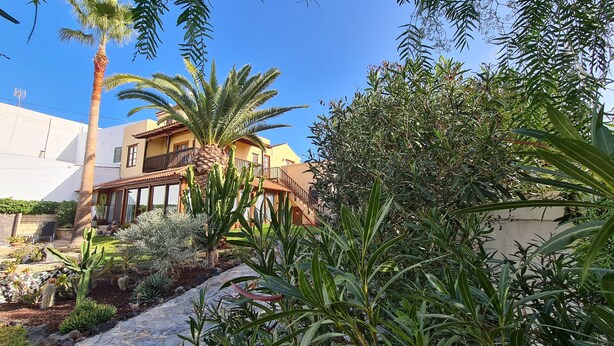 A two-story house with a balcony, surrounded by various cacti and plants. - A cozy blend of tranquility, beauty and functionality (Chío)