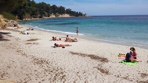 Ein Strand mit badenden Personen, blauem Himmel und ruhiger See.