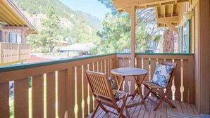 Terraza de madera con dos sillas y una mesa, con vistas a un paisaje montañoso.