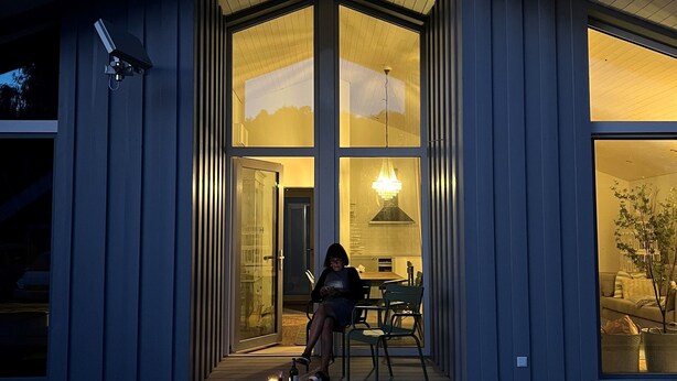 A modern house with large windows, a wooden deck, and a person sitting on a chair. - Lovingly furnished vacation home in the immediate vicinity of the lake (Mirow OT Granzow)