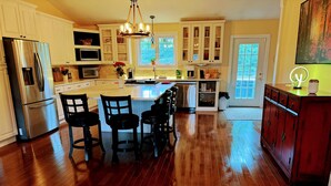 A spacious kitchen with wooden flooring, white cabinets, a stainless steel refrigerator, and a central island with bar stools. - Couples Villa Retreat w/85” Sony HD 8K TV Pool table New Jacuzzi Spa & Game room (Conway)