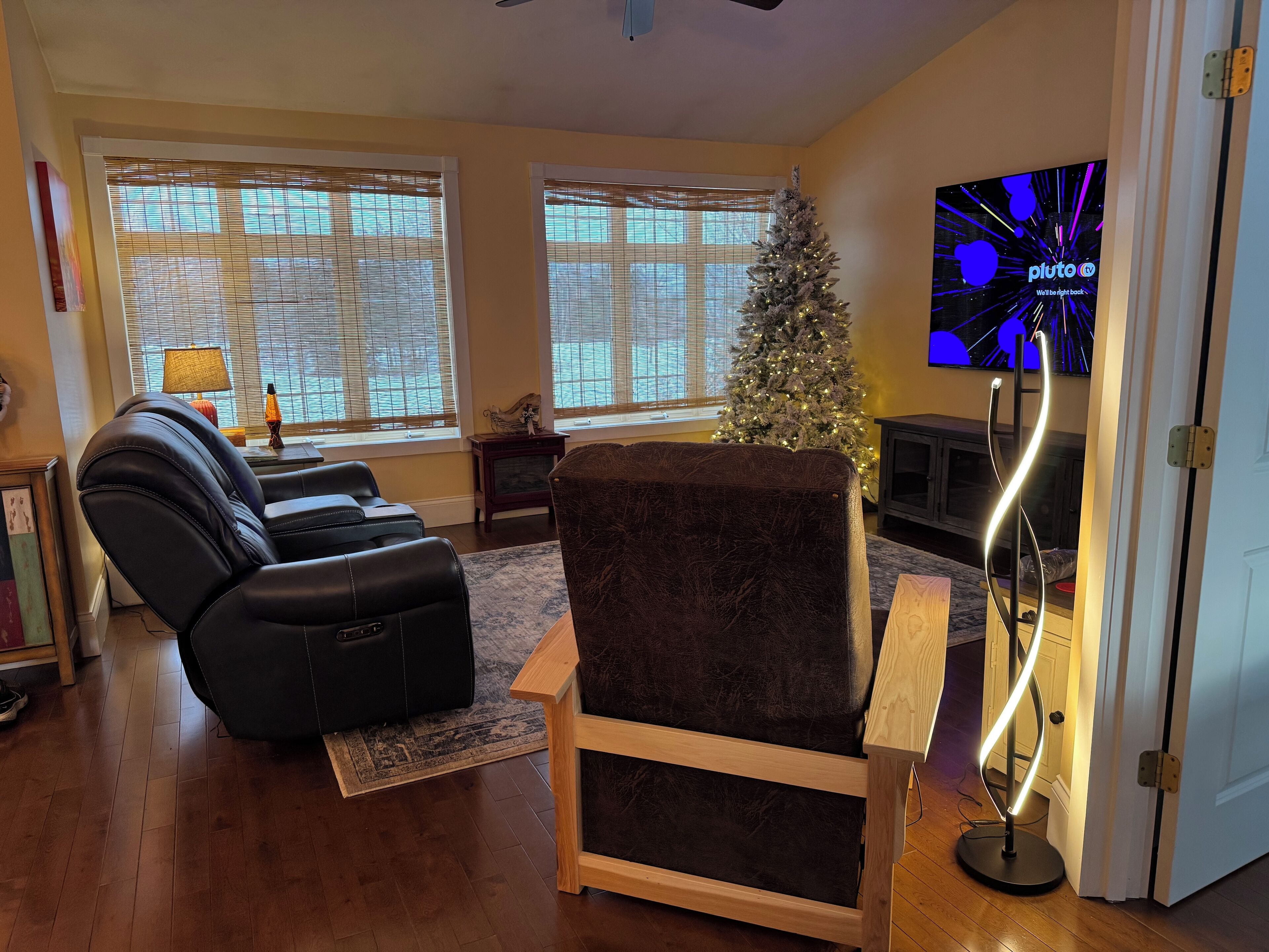 Una sala de estar con un sofá de cuero negro, una silla de madera, un árbol de Navidad y un televisor que muestra 'plutoo' en la pantalla.