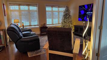 Una sala de estar con un sofá de cuero negro, una silla de madera, un árbol de Navidad y un televisor que muestra 'plutoo' en la pantalla.