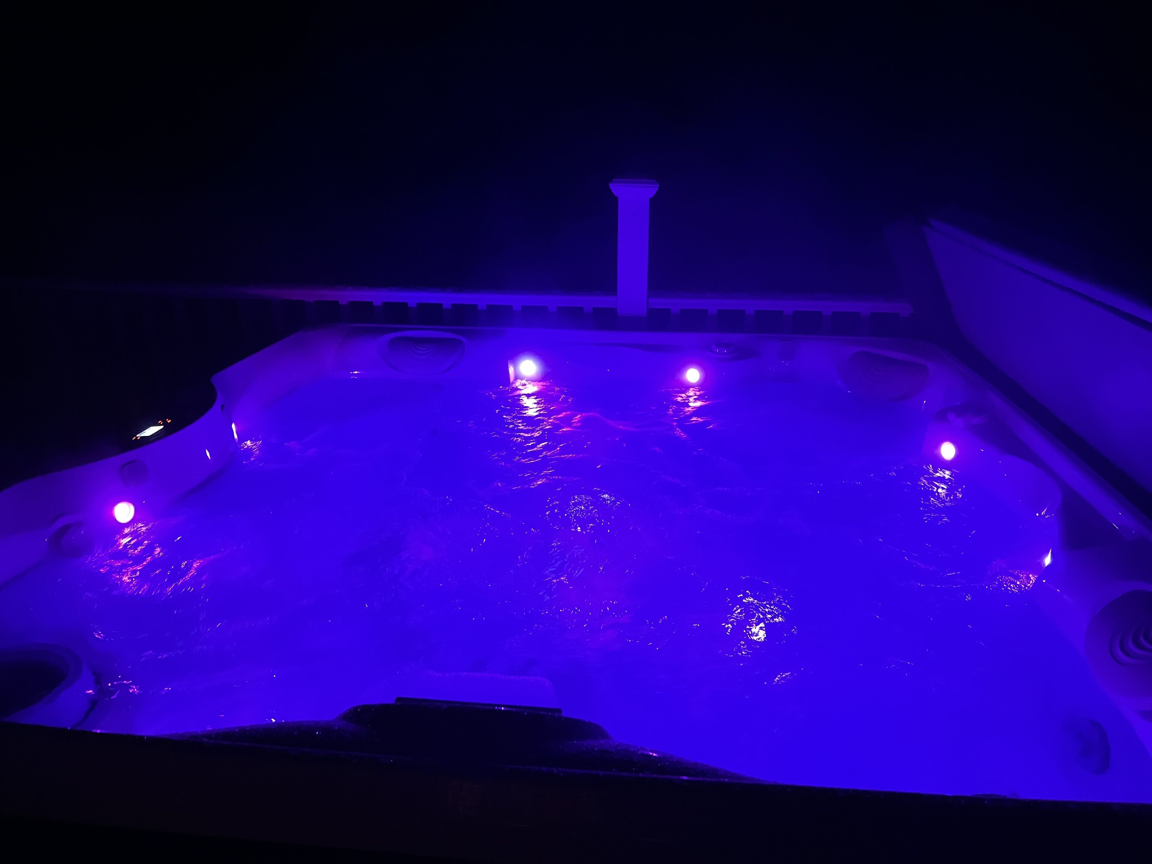 Ein Whirlpool mit violetter Beleuchtung, umgeben von einer dunklen Umgebung.