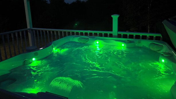 A hot tub with green lighting, surrounded by a deck with a railing. - Couples Villa Retreat w/85” Sony HD 8K TV Pool table New Jacuzzi Spa & Game room (Conway)