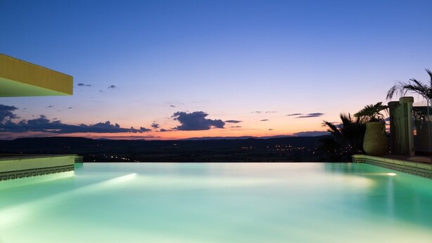 A serene infinity pool at dusk with a clear view of the horizon and distant city lights. - Magnificent Gite with dominant view swimming pool and jacuzzi (L'Olivier) (Langlade)