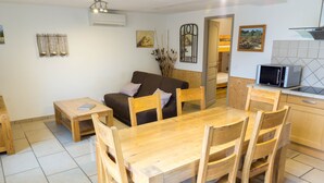 A cozy living area with a wooden dining table, chairs, a sofa, and a kitchen area with a microwave. - Magnificent Gite with dominant view swimming pool and jacuzzi (L'Olivier) (Langlade)