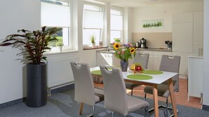 Una cocina moderna con armarios blancos, un comedor con mesa y sillas, y un amplio ventanal con persianas.