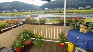 Una terraza con macetas y una mesa con mantel, con vistas a un río y casas al fondo.