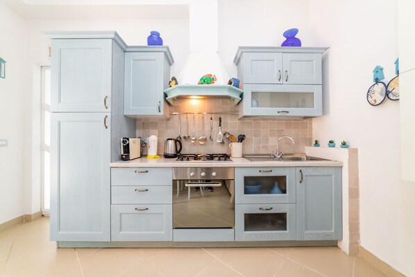 A kitchen with light blue cabinets, a stove, a sink, and a window.