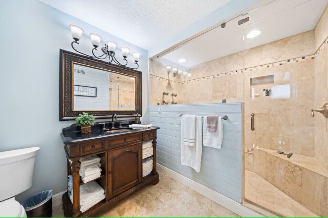 Een badkamer met een wastafel, een grote spiegel, een douche met glazen deur en een handdoekhouder.