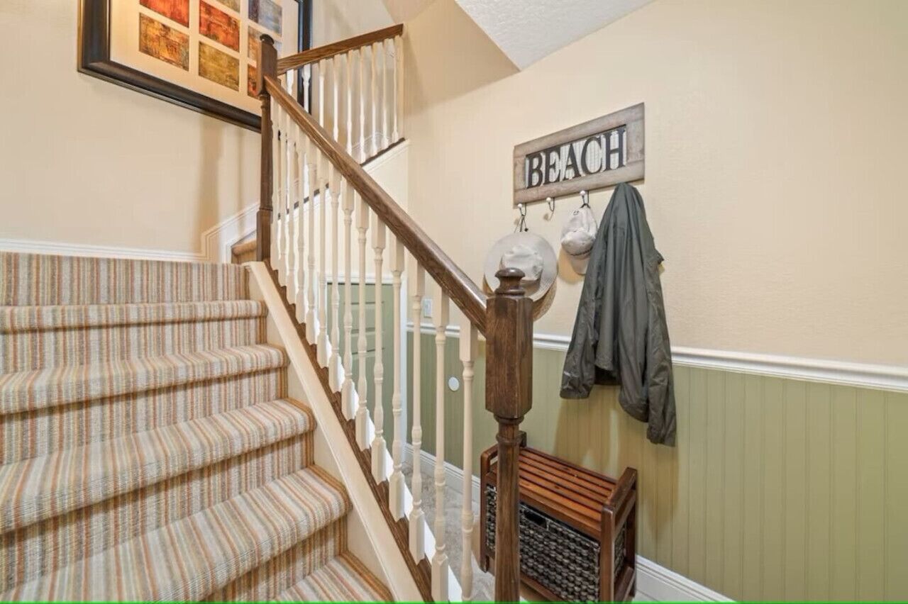 Un escalier recouvert d’une moquette à rayures, une main courante en bois et une enseigne fixée au mur sur laquelle on peut lire « PLAGE ».