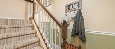 Un escalier recouvert d’une moquette à rayures, une main courante en bois et une enseigne fixée au mur sur laquelle on peut lire « PLAGE ».