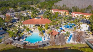 An aerial view of a resort with a central swimming pool, multiple buildings, and a surrounding natural landscape. - Perfect Getaway-4Bdrm Villa W/Pool in Gated Resort (Kissimmee)