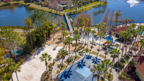 An aerial view of a resort area with a basketball court, palm trees, a lake, and a bridge. - Perfect Getaway-4Bdrm Villa W/Pool in Gated Resort (Kissimmee)